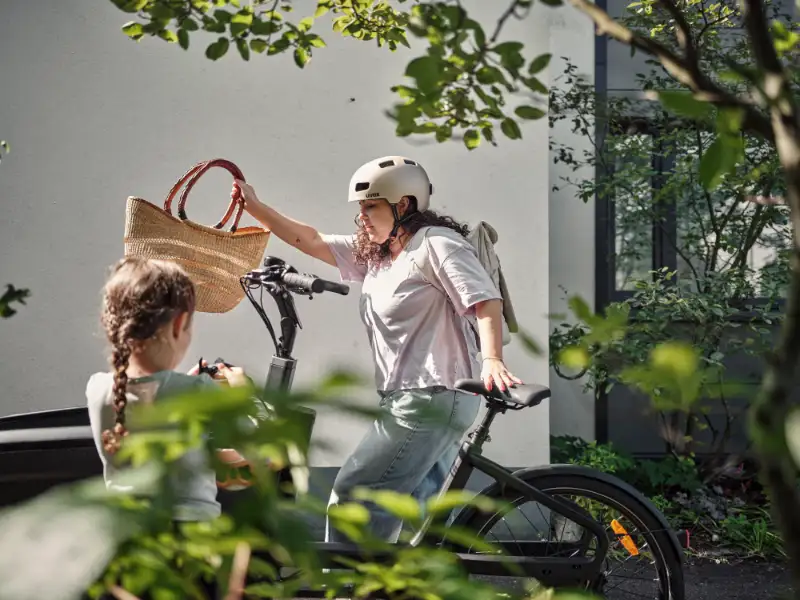 Eine Frau holt einen Korb aus dem Lastenrad, im Vordergrund schaut ein Kind zu Eine Frau holt einen Korb aus dem Lastenrad, im Vordergrund schaut ein Kind zu