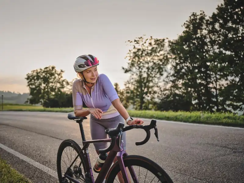 Rennradlerin lehnt entspannt am Rad in der Abendsonne