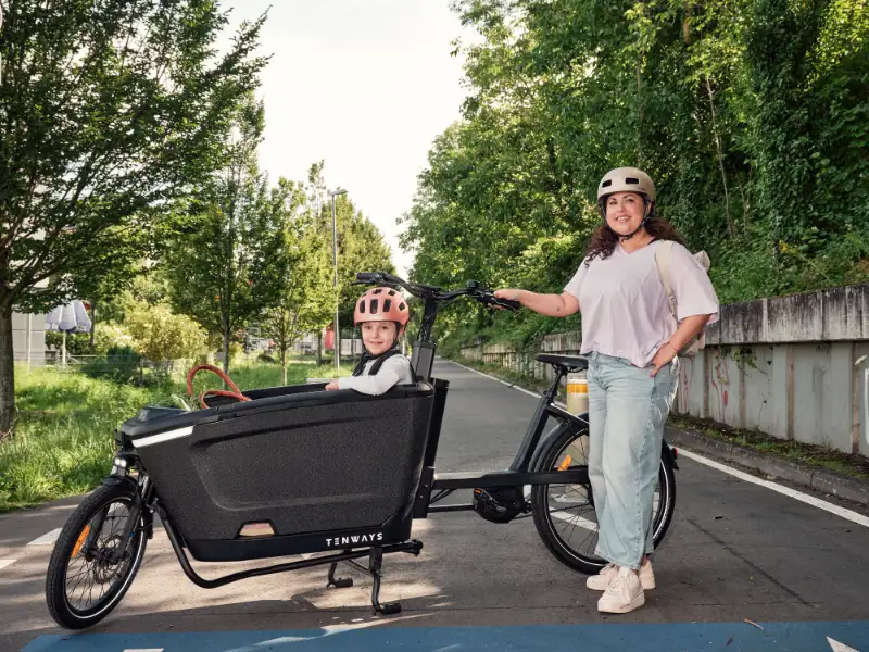 JobRadlerin posiert stolz neben ihrem Lastenrad mit Kind auf der Fahrradstraße