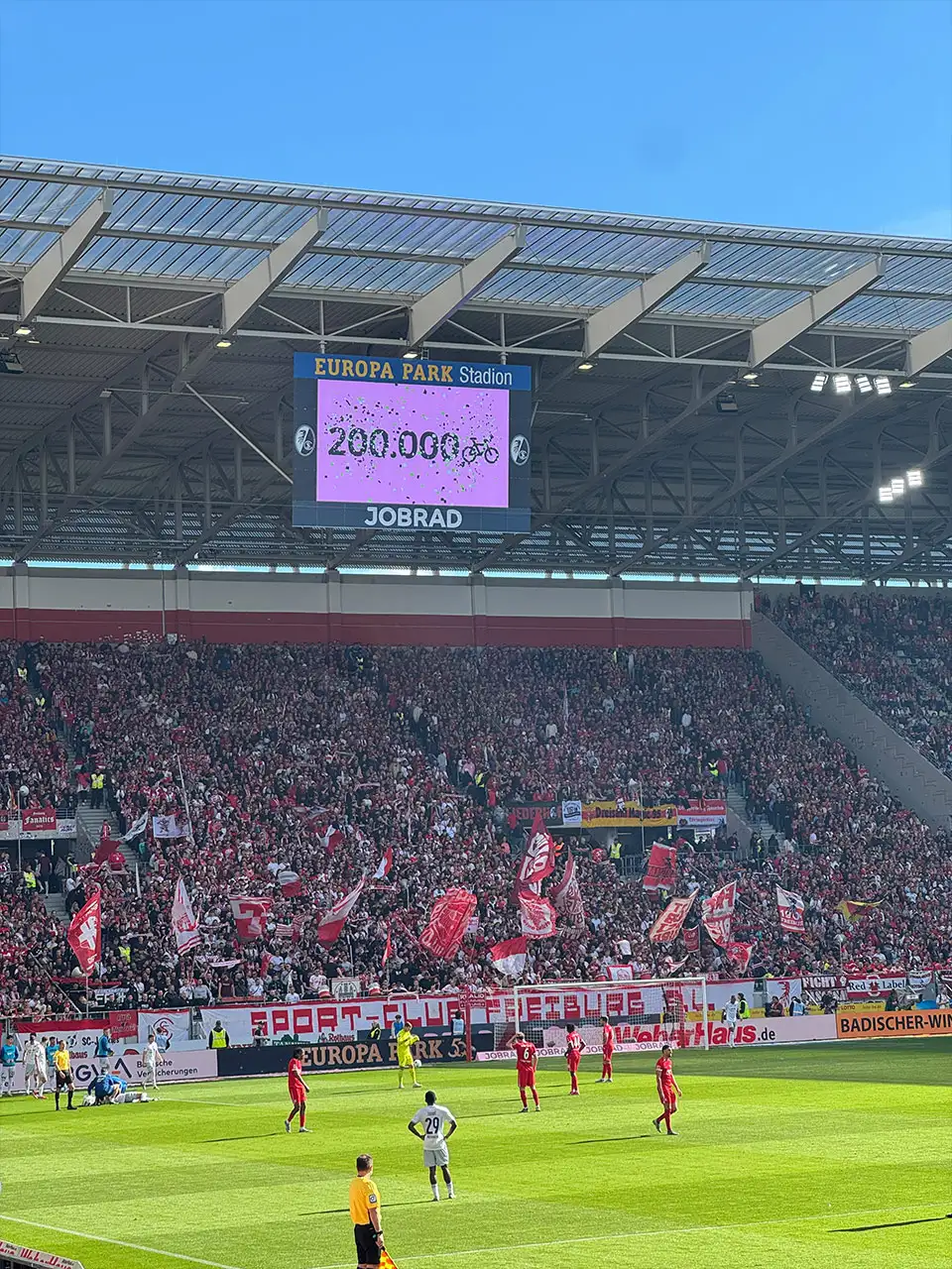 Der Screen im Europa-Park Stadion zeigt an, dass die 200.000 Fahrrad-Fan-Zahl erreicht wurde. Davor sieht man Spieler auf dem Spielfeld. Der Screen im Europa-Park Stadion zeigt an, dass die 200.000 Fahrrad-Fan-Zahl erreicht wurde. Davor sieht man Spieler auf dem Spielfeld.